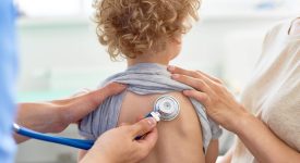 Unrecognizable male pediatrician examining curly little patient with help of stethoscope, blurred background