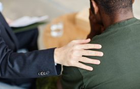 Unrecognizable professional psychologist comforting Black soldier suffering depression touching his shoulder